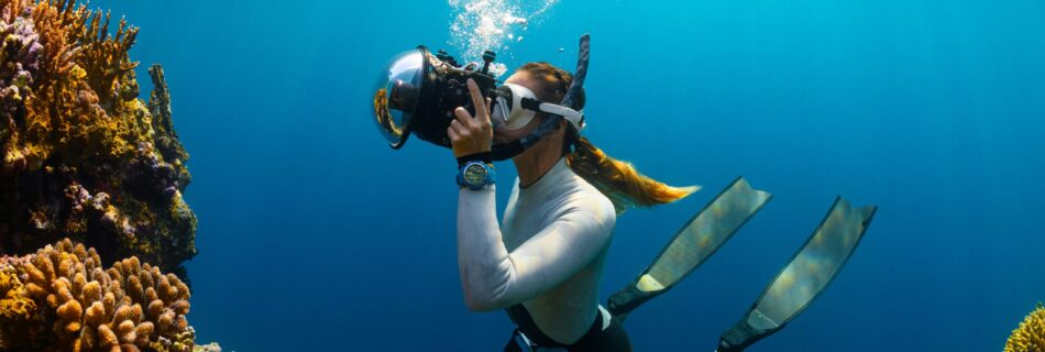 a woman scubas in the ocean with a camera